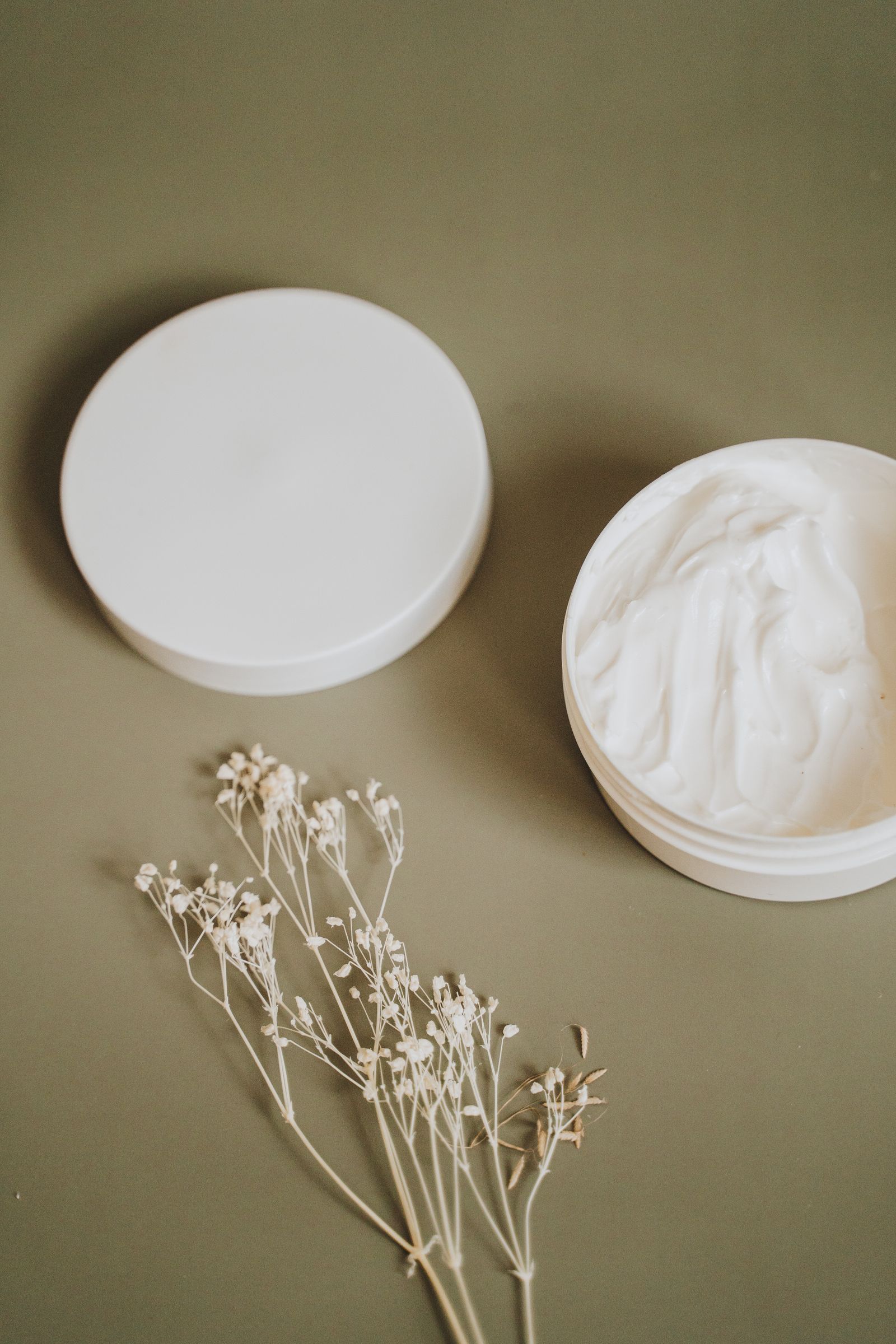 Tarro abierto de crema natural sin marca sobre una superficie verde