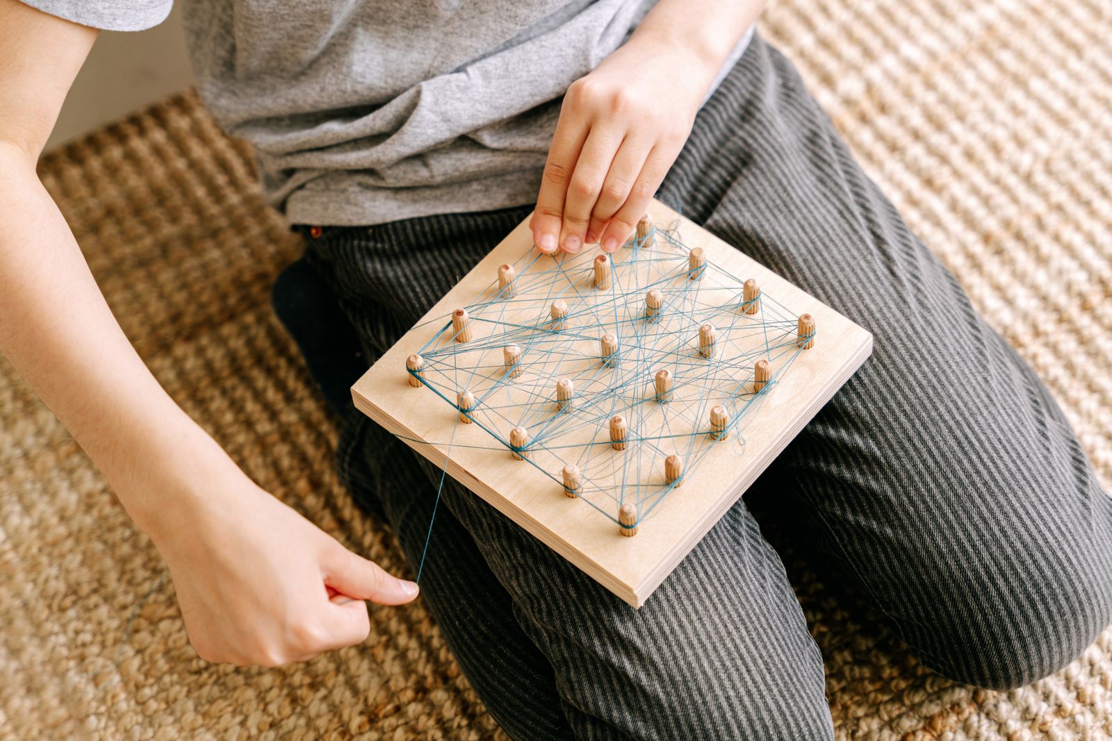 Niño creando formas con elásticos sobre un tablero de madera con clavijas